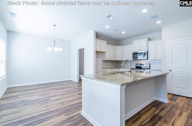 kitchen featuring white cabinetry, light stone countertops, stainless steel appliances, wood-type flooring, and a center island with sink