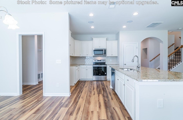 kitchen featuring white cabinets, sink, hardwood / wood-style flooring, light stone counters, and stainless steel appliances