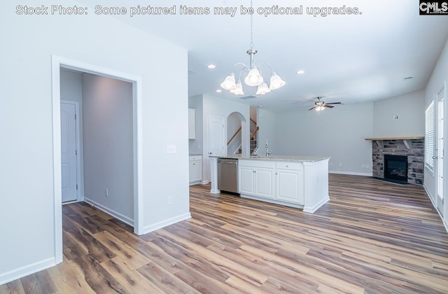 kitchen featuring hanging light fixtures, stainless steel dishwasher, wood-type flooring, a fireplace, and white cabinets