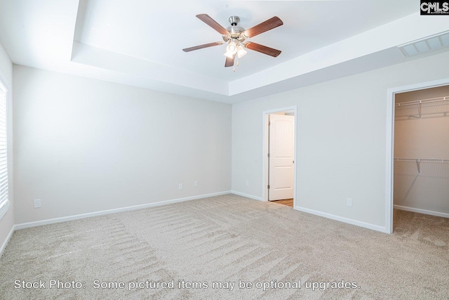 unfurnished bedroom with a raised ceiling, a walk in closet, and light carpet