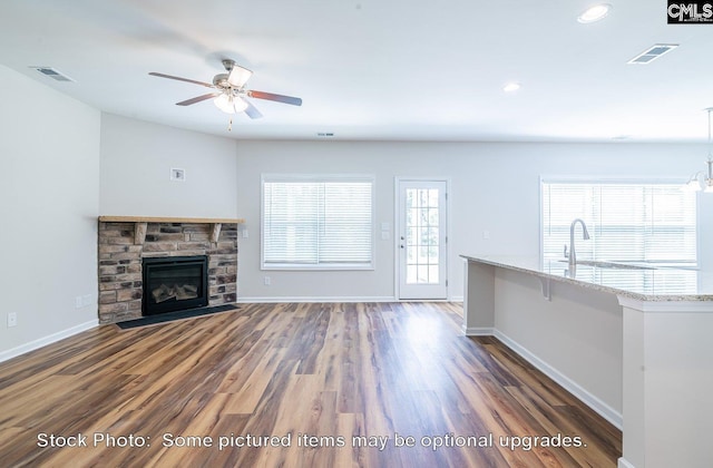 unfurnished living room with a stone fireplace, dark hardwood / wood-style flooring, and ceiling fan with notable chandelier