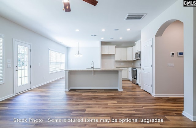 kitchen featuring appliances with stainless steel finishes, light stone counters, a center island with sink, white cabinets, and dark hardwood / wood-style floors