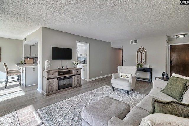 living room featuring sink, a textured ceiling, and light wood-type flooring