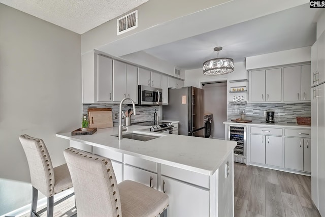 kitchen featuring kitchen peninsula, light wood-type flooring, stainless steel appliances, wine cooler, and hanging light fixtures