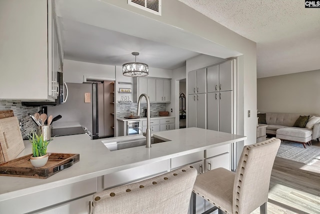 kitchen featuring kitchen peninsula, backsplash, a textured ceiling, decorative light fixtures, and light hardwood / wood-style floors