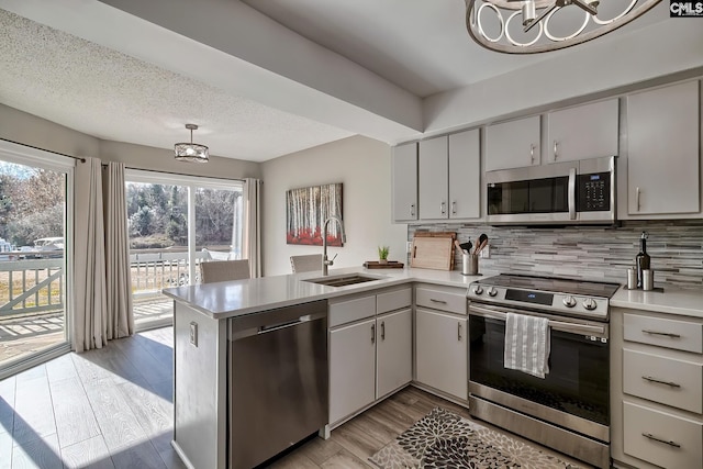 kitchen with kitchen peninsula, stainless steel appliances, sink, decorative light fixtures, and light hardwood / wood-style floors