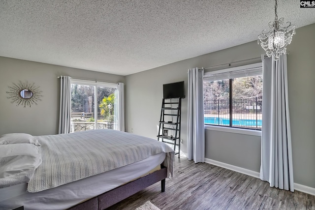 bedroom with multiple windows, hardwood / wood-style floors, a textured ceiling, and an inviting chandelier