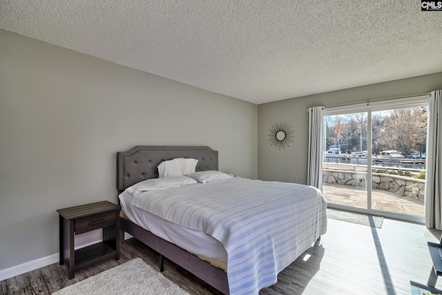 bedroom with access to exterior, a textured ceiling, and hardwood / wood-style flooring