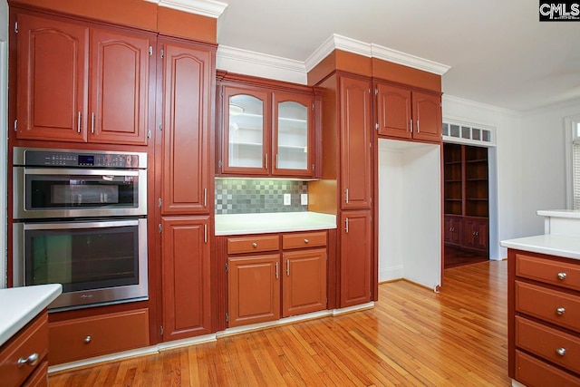 kitchen featuring decorative backsplash, stainless steel double oven, light hardwood / wood-style flooring, and crown molding