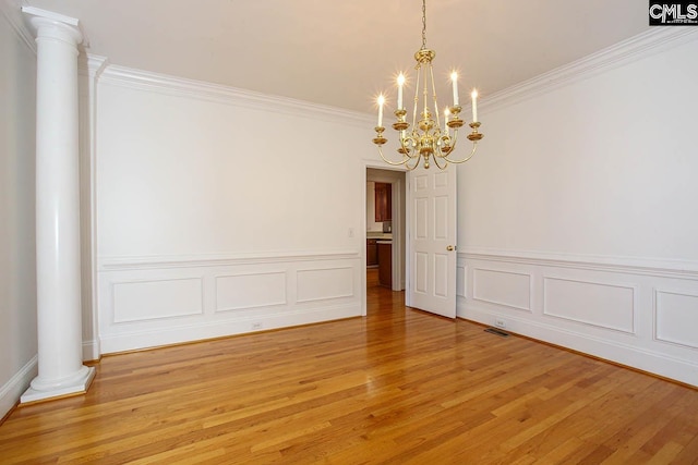 spare room featuring ornate columns, crown molding, a chandelier, and light wood-type flooring