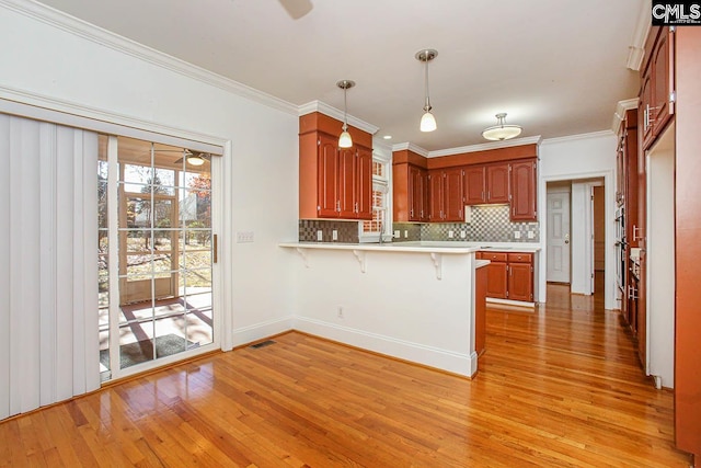 kitchen with kitchen peninsula, a kitchen bar, light wood-type flooring, crown molding, and decorative light fixtures