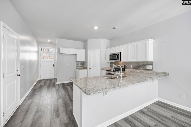 kitchen with sink, appliances with stainless steel finishes, kitchen peninsula, white cabinets, and backsplash