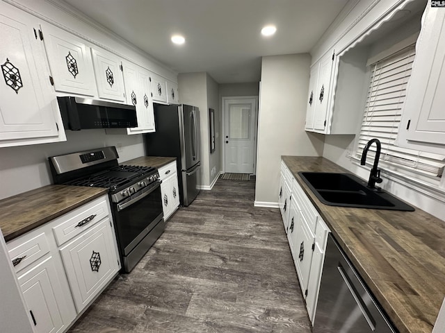 kitchen with stainless steel appliances, dark wood-type flooring, sink, white cabinetry, and butcher block counters