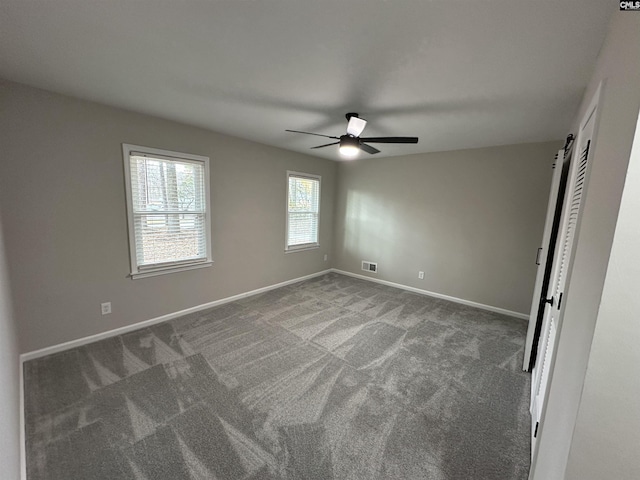 unfurnished bedroom featuring dark colored carpet, a barn door, and ceiling fan