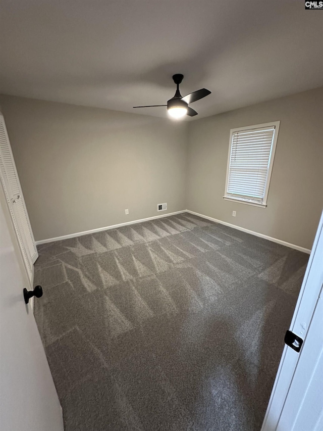 empty room featuring ceiling fan and dark colored carpet