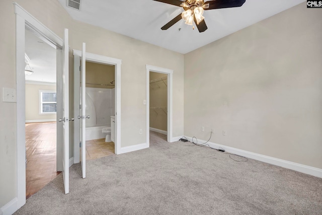 unfurnished bedroom with light carpet, a walk in closet, ensuite bathroom, ceiling fan, and a closet