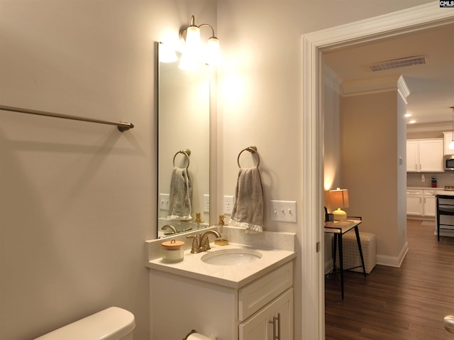 half bathroom with visible vents, toilet, ornamental molding, vanity, and wood finished floors