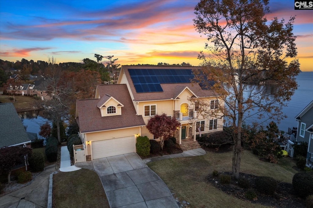 view of front of house with solar panels, a garage, a water view, and a yard