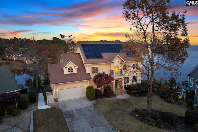 view of front of house with solar panels, a garage, a water view, and a yard