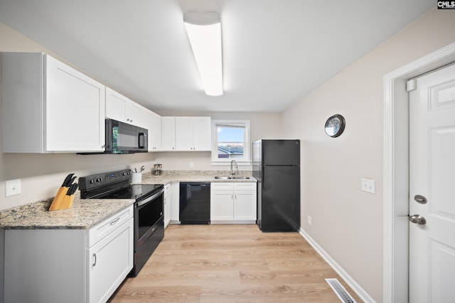 kitchen with black appliances, white cabinets, sink, light stone countertops, and light hardwood / wood-style floors