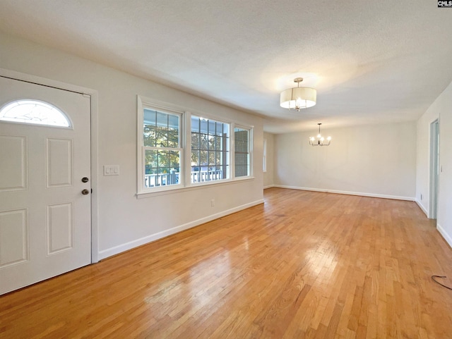 entryway with light hardwood / wood-style floors, a textured ceiling, and a notable chandelier