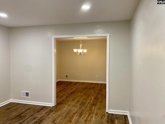 unfurnished room with a chandelier and dark wood-type flooring