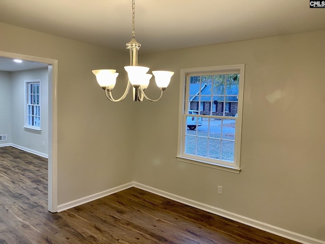 unfurnished dining area featuring a chandelier and dark wood-type flooring