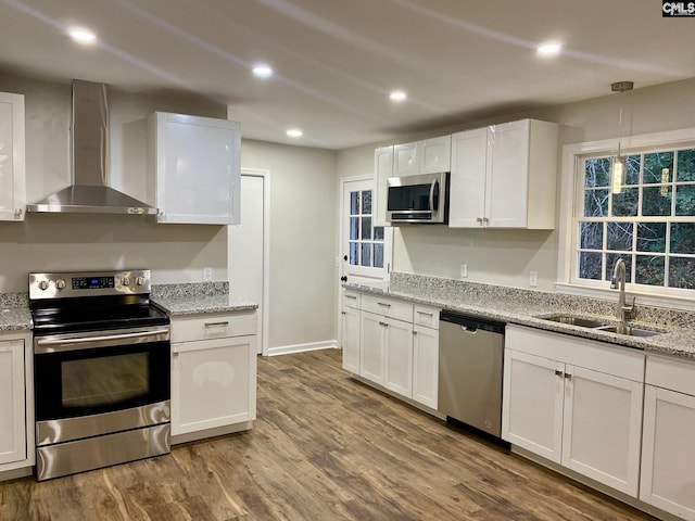 kitchen with sink, wall chimney range hood, appliances with stainless steel finishes, white cabinets, and hardwood / wood-style flooring