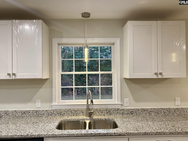 kitchen with white cabinets, pendant lighting, light stone countertops, and sink