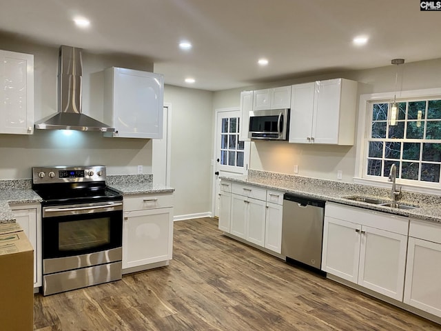 kitchen featuring sink, wall chimney exhaust hood, wood-type flooring, white cabinets, and appliances with stainless steel finishes