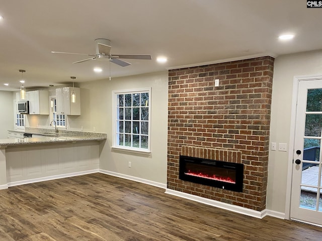 unfurnished living room featuring dark hardwood / wood-style floors, a brick fireplace, ceiling fan, and sink