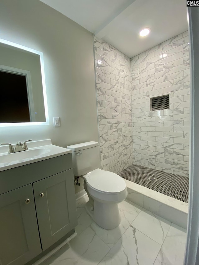 bathroom with a tile shower, vanity, and toilet