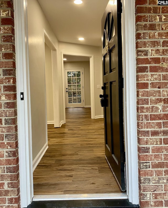 hallway featuring dark wood-type flooring and brick wall