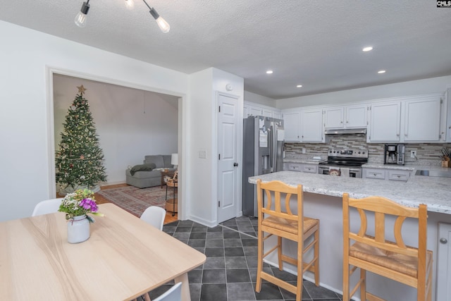 kitchen with a kitchen bar, tasteful backsplash, a textured ceiling, stainless steel appliances, and white cabinetry