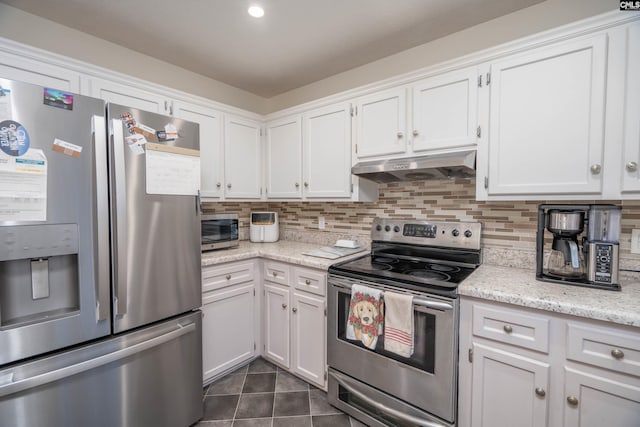 kitchen with light stone countertops, appliances with stainless steel finishes, backsplash, dark tile patterned floors, and white cabinetry