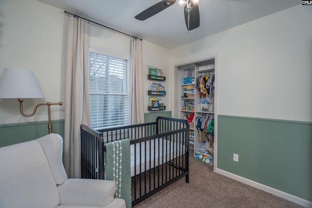 carpeted bedroom with a crib, a textured ceiling, a closet, and ceiling fan