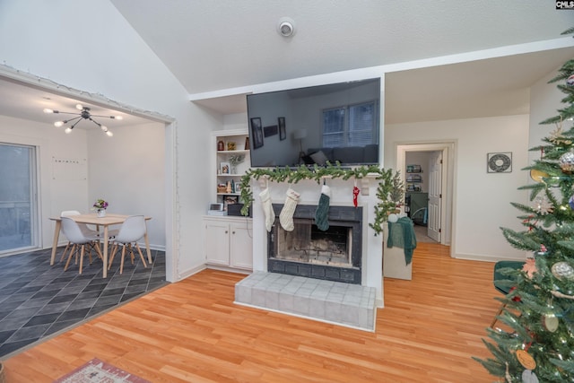 living room with hardwood / wood-style floors, a notable chandelier, vaulted ceiling, and a tiled fireplace