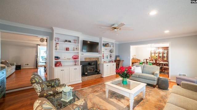 living room with light wood-type flooring, a wood stove, ceiling fan, and ornamental molding