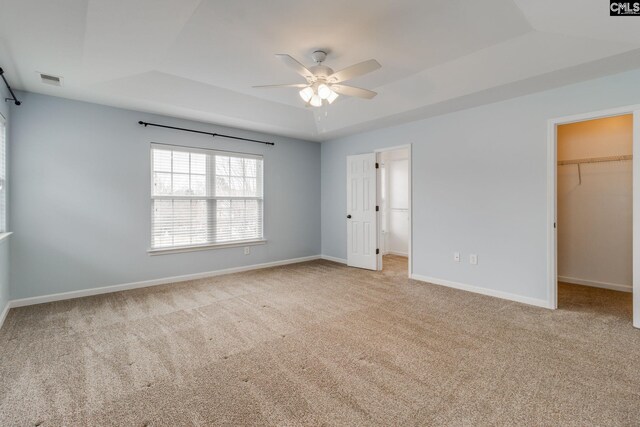 unfurnished bedroom featuring a spacious closet, ceiling fan, a raised ceiling, light colored carpet, and a closet