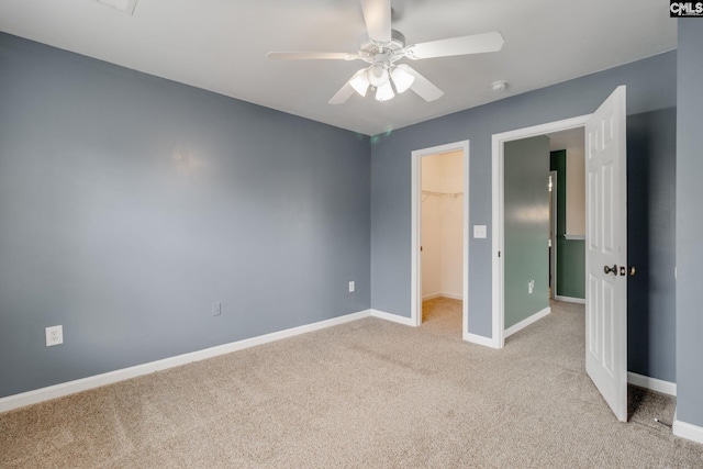 unfurnished bedroom featuring light carpet, a closet, a spacious closet, and ceiling fan