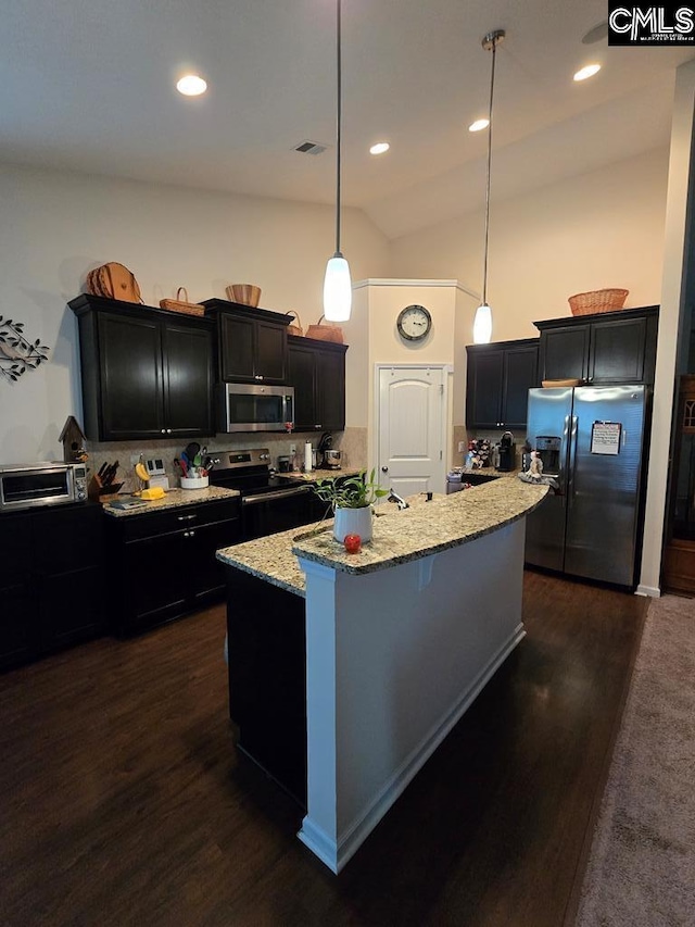 kitchen featuring dark wood-type flooring, vaulted ceiling, an island with sink, appliances with stainless steel finishes, and decorative light fixtures