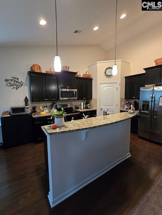 kitchen with dark wood-type flooring, lofted ceiling, decorative light fixtures, a center island with sink, and appliances with stainless steel finishes