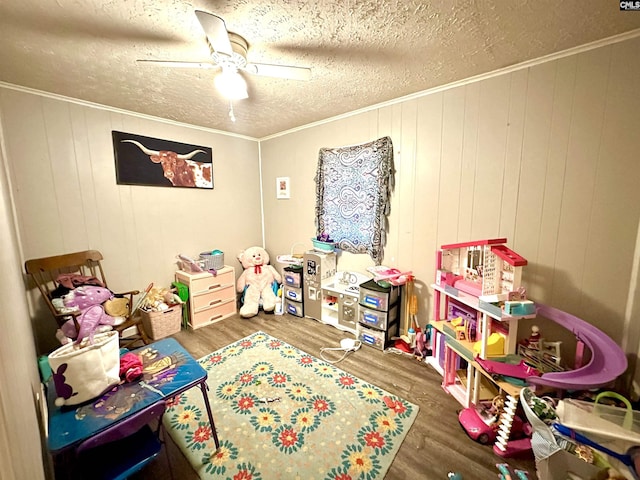 rec room with wood walls, ceiling fan, wood-type flooring, and ornamental molding