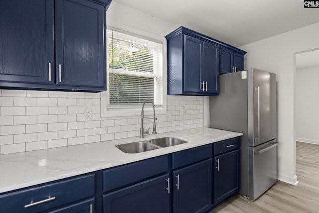 kitchen with sink, tasteful backsplash, light hardwood / wood-style flooring, blue cabinets, and stainless steel fridge