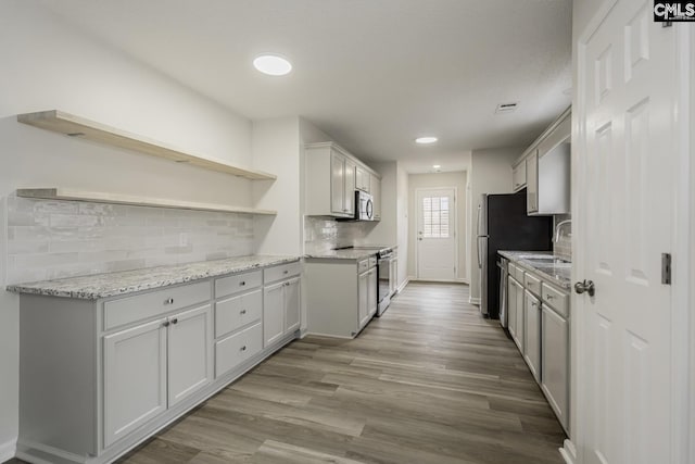 kitchen with light stone countertops, stainless steel appliances, tasteful backsplash, white cabinets, and light wood-type flooring