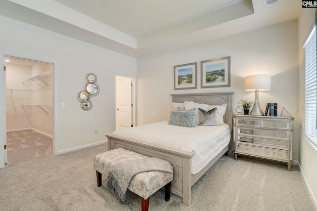 bedroom featuring light carpet, a tray ceiling, a spacious closet, and a closet