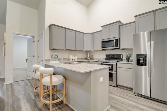 kitchen with kitchen peninsula, light stone counters, stainless steel appliances, sink, and a high ceiling