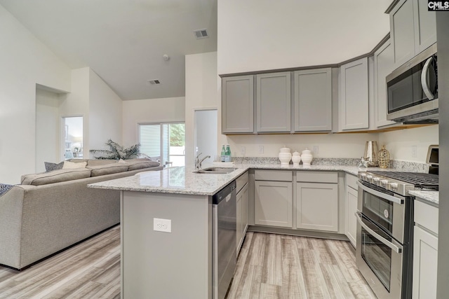 kitchen with kitchen peninsula, light wood-type flooring, light stone counters, stainless steel appliances, and sink