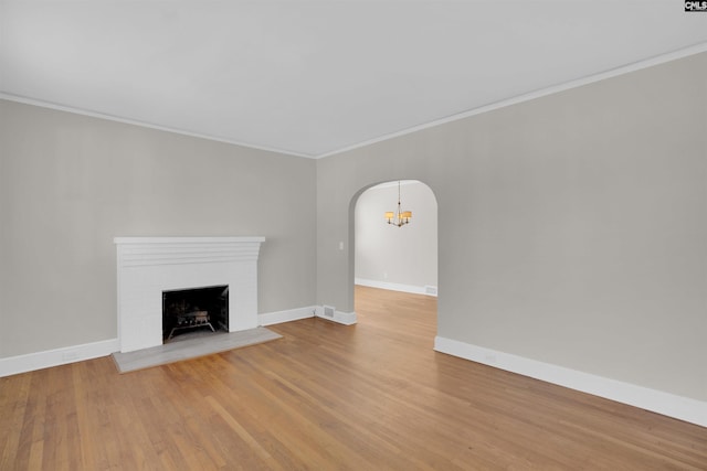 unfurnished living room with a fireplace, light wood-type flooring, crown molding, and a notable chandelier