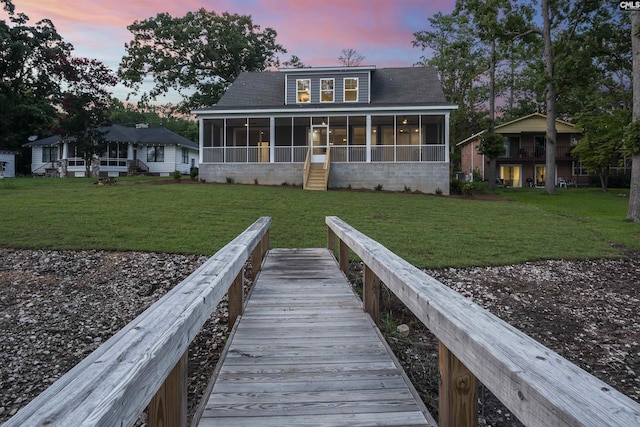 back house at dusk featuring a lawn and a sunroom